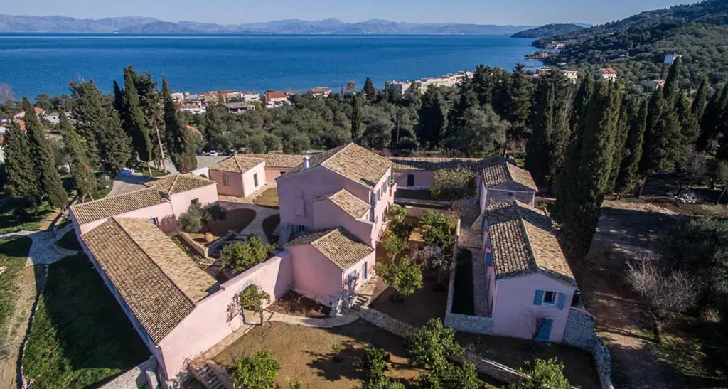 Aerial view of The Courti Estate, a hilltop villa set in a large green open space with the sea in the background.
