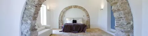 A Courti Estate Bedroom with stone archway, white walls and dtone flooring.